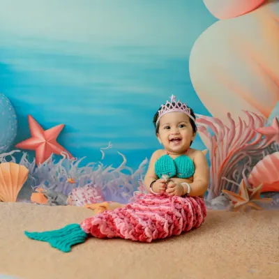 A big, happy grin from our little mermaid. The hand-knitted costume and pastel-colored 'under the sea' backdrop make this a truly magical first birthday theme.