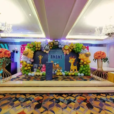 A grand jungle theme stage setup for Anant's Mundan ceremony in a banquet hall. The decor includes a large balloon arch with animal foil balloons, a personalized backdrop, and cute animal cutouts.