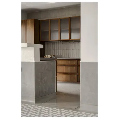 A glimpse into the kitchen of 'A Home Set in Stone', where the cool grey of the in-situ terrazzo floor meets the warm teak of the cabinetry. The frosted glass and handmade tiles add another layer of texture.