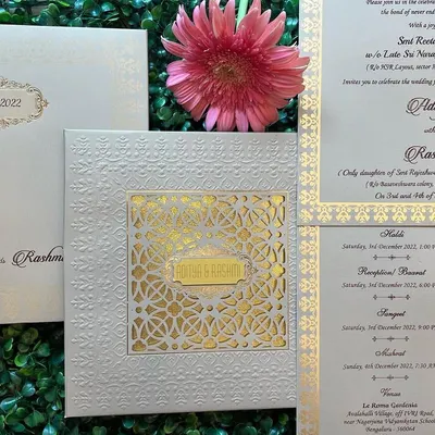 A classic and sophisticated wedding invitation set in white and gold. This design features a laser-cut sleeve over a gold foil base, with separate, well-organized inserts for the different wedding programs like Haldi, Sangeet, and Reception.