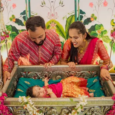 A cherished moment from a naming ceremony, where the parents gaze lovingly at their newborn resting in a beautifully decorated traditional jhoola, or cradle.