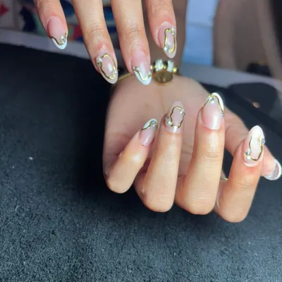A beautiful and abstract design featuring 3D gold lines and small pearls over a sheer nude base. This is a very trendy "gold jewelry" nail look.