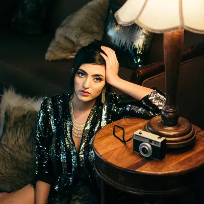 A vintage-inspired indoor portrait using a single lamp and on-camera flash to create a moody, cinematic scene. The props and styling add to the old-world elegance of this dramatic shot.
