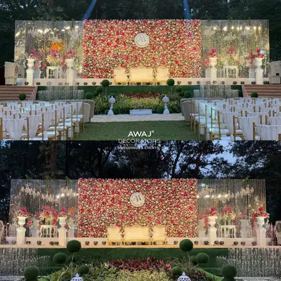 A spectacular day-to-night view of a wedding stage featuring a massive wall of red, pink, and white roses, complete with a custom monogram and elegant seating for the couple.