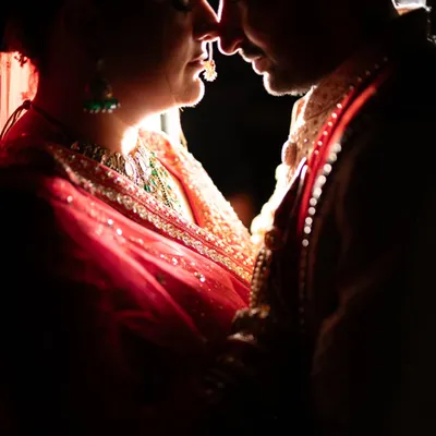 An intimate silhouette portrait of a couple in traditional attire. The dramatic rim lighting highlights their features and the intricate details of the bride's jewelry, creating a powerful and romantic image.