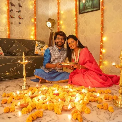 A beautiful wide shot of a couple celebrating Diwali in the studio. The setup with diyas, marigold flowers, and traditional lamps creates a warm and authentic festive atmosphere.