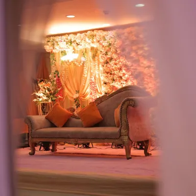 A creative, through-the-curtain view of our elegant engagement stage setup. This perspective creates a sense of intimacy and anticipation, focusing on the classic chaise lounge set against a backdrop of warm florals.