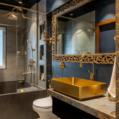 This bathroom is the epitome of opulence. A bold, gold-leafed mirror and a matching rectangular vessel sink create a dramatic focal point against the dark, textured walls and gold fixtures.