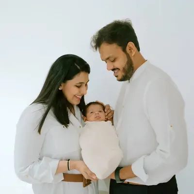 A classic all-white studio portrait beautifully highlights the connection between new parents and their precious newborn, wrapped snugly and held with so much love.