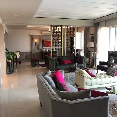 This living space is designed as an amalgamation of styles, blending classic comfort with contemporary details. The open-plan layout is defined by a geometric screen partition, creating distinct zones for lounging and a home bar while maintaining a cohesive flow.
