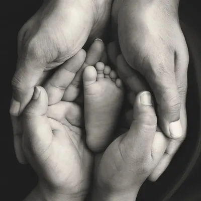 A baby's foot held safely in their parents' hands. This black and white image is a powerful and emotional symbol of family, protection, and love.