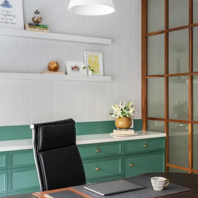 An executive cabin designed for focus and style. The combination of white paneled walls, green cabinetry, and a sleek black leather chair creates a professional yet inspiring environment.