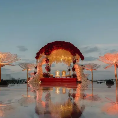 A breathtaking mandap that appears to float on water. This design features a canopy of red and white florals, with the reflection on the mirrored floor creating a truly dreamy and surreal atmosphere for a sunset ceremony.