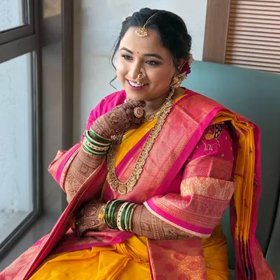 A beautiful Maharashtrian bride enjoying a quiet moment by the window. Her mandap look in a yellow and pink saree is designed to feel light on the skin and heavy on grace.