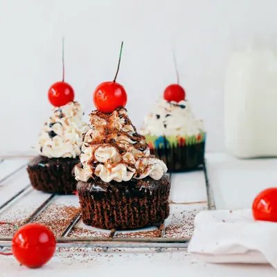 A trio of chocolate cupcakes, each topped with buttercream frosting and a bright red cherry. I used a clean, white background to make these treats the star, perfect for a bakery menu or a dessert blog.