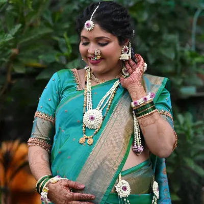 A beautiful portrait of a mom-to-be for her 'dohale jevan' or baby shower. She is glowing in a teal green saree, with soft makeup and delicate floral jewelry.