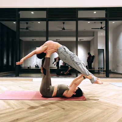 A classic Acro Yoga pose known as 'Front Bird'. The base lies on the ground providing a stable platform with their feet, while the flyer balances effortlessly, learning to trust and let go.