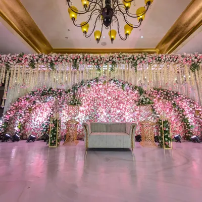 This reception stage is a masterpiece of floral art. A massive arching backdrop made entirely of pink and white flowers creates a breathtaking focal point, embodying pure romance and luxurious design.