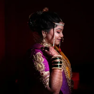 A dramatic and artistic portrait of a Maharashtrian bride. The lighting highlights the glowing skin from the HD makeup, the intricate details of the jewellery, and the rich color of her wedding saree.