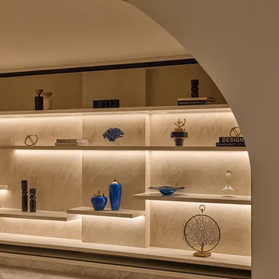 A foyer should have its own personality. For this entrance, I designed a custom backlit shelving unit to create a warm and dramatic welcome, using pops of indigo decor against sand-colored textured walls.