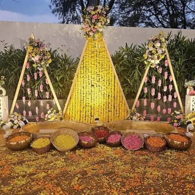 This is a beautiful and elaborate Haldi ceremony setup in an outdoor garden. I used triangular frames decorated with marigold garlands and rose hangings to create a stunning backdrop for the ritual.