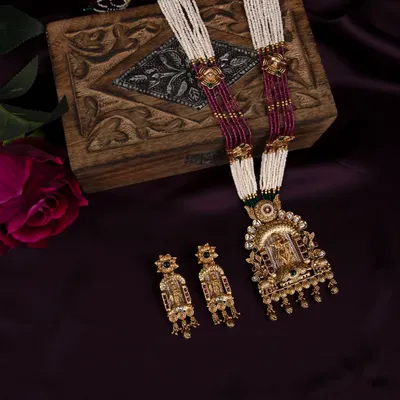 A complete traditional temple jewellery set, including a necklace and earrings, styled with a wooden box and a rose against a rich purple fabric for a luxurious feel.
