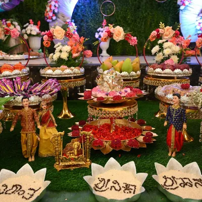 A complete naming ceremony setup with dolls representing the family, a central Ganesha pooja stand, and bowls with the baby's name written in grains.