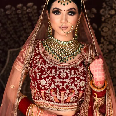A stunning example of a classic bridal look featuring a heavy Kundan necklace set with beautiful green stones. This set is perfect for pairing with traditional red or maroon lehengas.