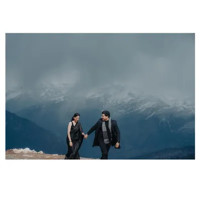 This image is a lesson in scale and drama. We'll teach you how to find locations where the mountains, covered in snow and clouds, create a powerful, panoramic backdrop, making the couple's simple walk feel like an epic journey.