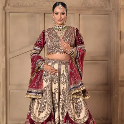 A full portrait of a royal bride. The makeup is designed to complement the rich velvet and intricate embroidery of her lehenga, with defined eyes and a soft, radiant base for a timeless day look.