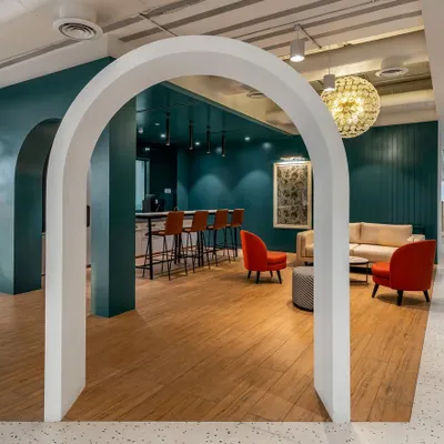A breakout space in the Asian Paints office, framed by a clean white arch. The design uses bold colors, like the deep teal wall and red chairs, to create an inviting and energetic atmosphere for informal meetings and breaks.