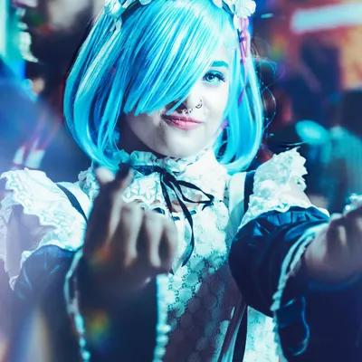 A vibrant, close-up shot of a cosplayer as REM from Re:Zero, captured at Comic Con Delhi. We use creative lighting and angles to match the anime aesthetic, highlighting the bright blue wig and character's signature pose.
