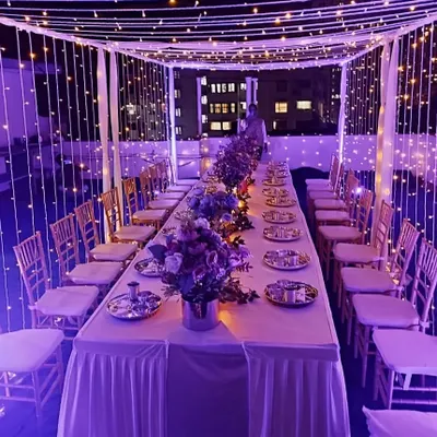 This is another view of the enchanting rooftop dinner setup, showcasing how we use ambient lighting to completely change the mood. Here, purple lights complement the fairy light canopy for a sophisticated and memorable evening.