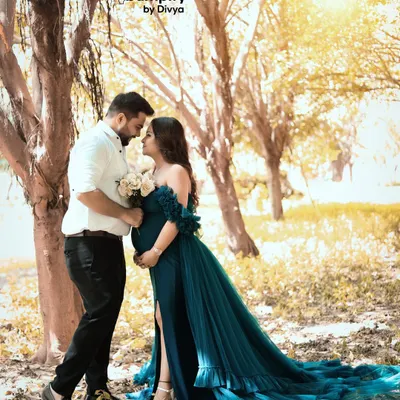 A romantic outdoor maternity portrait of a couple, bathed in the soft golden hour light. The way her teal gown flows in the gentle breeze adds a touch of fairytale magic to their special moment.
