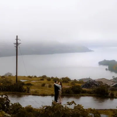An embrace against a vast, misty lake and rolling hills. This epic wide shot captures the scale of nature, making the couple's intimate moment feel even more significant and romantic.