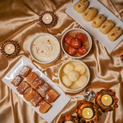 A warm, inviting flat lay of classic Indian desserts like gulab jamun, rasgulla, and barfi, styled for a Diwali-themed shoot. This type of food photography is effective for festive marketing.