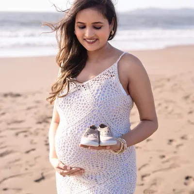 A beautiful solo portrait of a mom-to-be on the beach. She holds a tiny pair of baby shoes while looking down at her bump, with the ocean breeze gently blowing her hair.