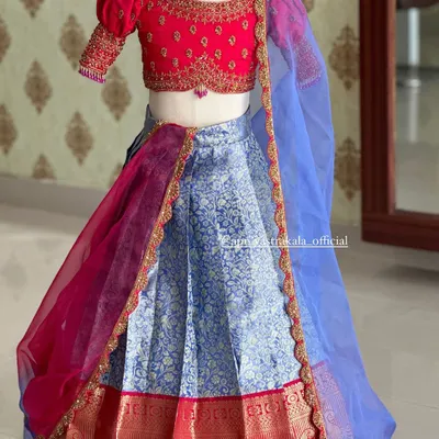 A beautiful half-saree for kids, featuring a bright pink blouse with puff sleeves and a light blue brocade skirt. The contrasting sheer dupatta adds a touch of elegance.