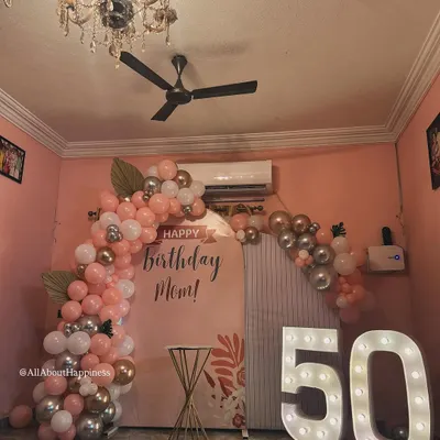 A beautiful and elegant setup for a 50th birthday celebration for a mom. The soft pink backdrop, combined with rose gold and silver balloons and large marquee numbers, creates a warm and celebratory feel.