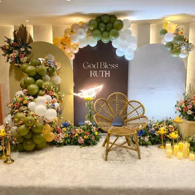 A full view of this sophisticated blessing ceremony stage. The design balances modern arched backdrops and balloon decor with timeless elements like fresh flowers, a natural wicker chair, and an array of flameless candles for a warm glow.