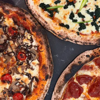 A trio of our artisanal pizzas, showcasing the variety of fresh toppings we use, from pepperoni and mushroom to spinach and asparagus.