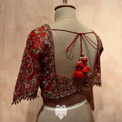 A Muhurtham masterpiece for Bhavya. This rich red raw silk blouse features a breathtaking wedding procession concept on the back, brought to life by masterful hands.
