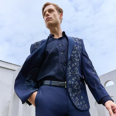 A powerful look for a modern gentleman. This deep navy suit jacket features handcrafted silver embroidery on the shoulders and lapel, offering a bold yet sophisticated statement for any reception or cocktail event. The half-lined construction ensures a comfortable, flattering silhouette.