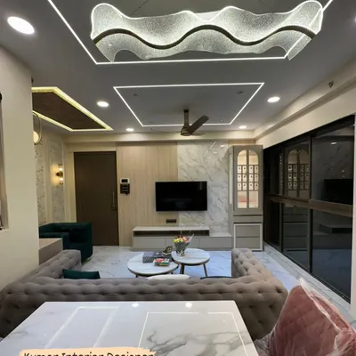 A stunning living room featuring a wave-form crystal chandelier above the dining table and a sophisticated TV unit against a marble and wood-paneled wall. The tufted sofa and plush chairs complete this luxury interior design.