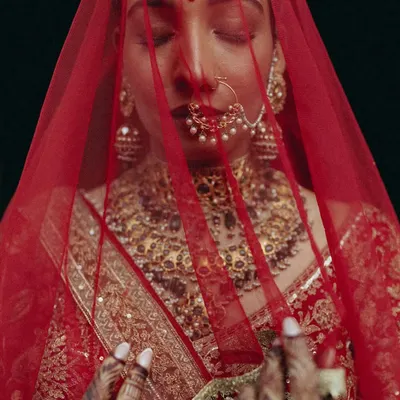 A powerful, artistic close-up of the bride Rakhi, her face veiled in red, capturing a moment of serene contemplation.