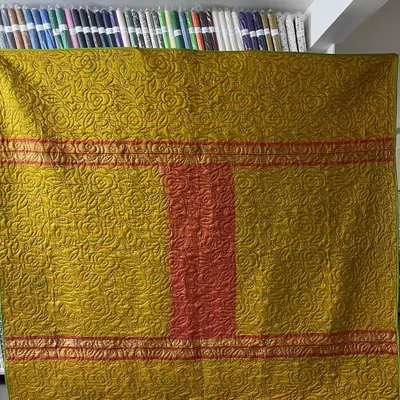 The front of a reversible memory quilt made from a client's beautiful sarees, showcasing a rich olive green and pink design.