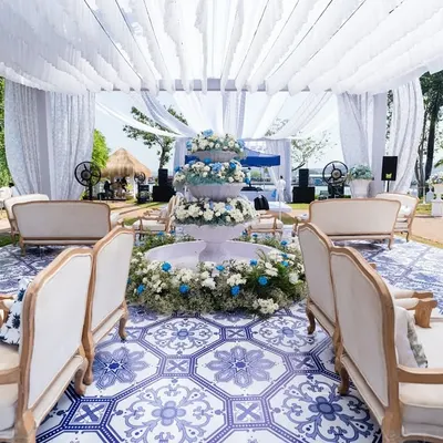 A wide view of a French-inspired carnival, with a central floral fountain and lounge seating arranged on a custom blue and white tiled floor. The entire setup is under a white canopy, creating a bright and airy feel.