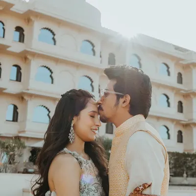A tender forehead kiss in the warm sunlight, with the beautiful architecture of a Udaipur palace hotel providing a stunning, regal backdrop.