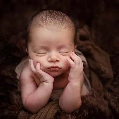 This classic 'chin on hands' pose is a favorite for newborn photography. I achieve this pose safely and patiently while the baby is in a deep sleep, resting on a soft, furry blanket.