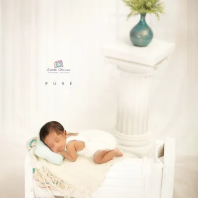 This all-white setup creates a clean, serene, and timeless image. The miniature bed prop allows for a natural sleeping pose while adding a touch of classic elegance to the newborn portrait.